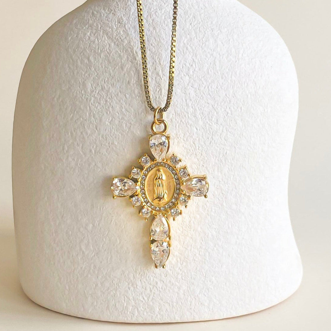 Colgante Cruz Circonitas Blancas de Bendita Eva en acero y oro mostrado en expositor. Circonitas de 2,5 mm y virgen grabada, diseño waterproof, hipoalergénico y duradero.