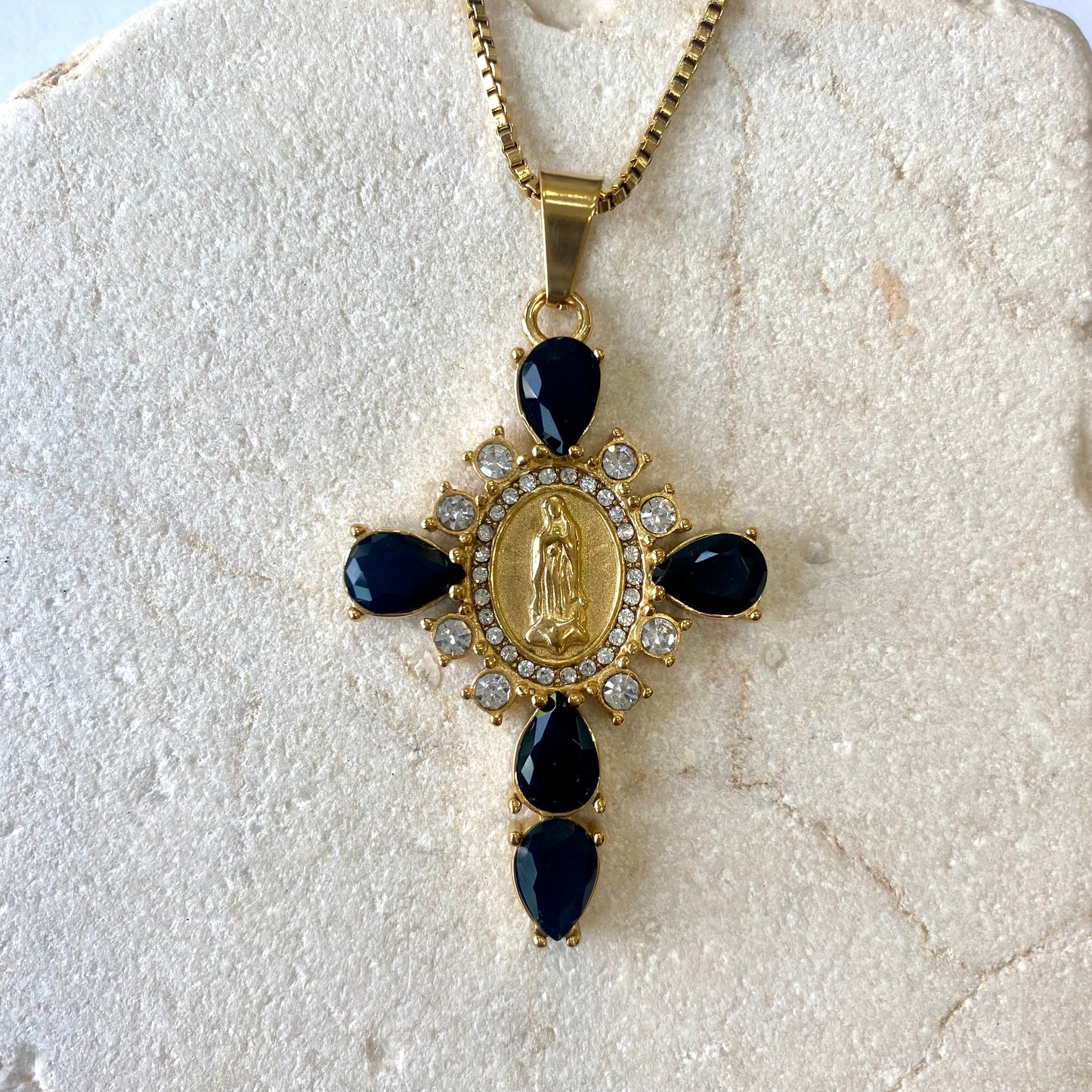 Colgante cruz con circonitas blancas y negras de Bendita Eva presentado sobre superficie