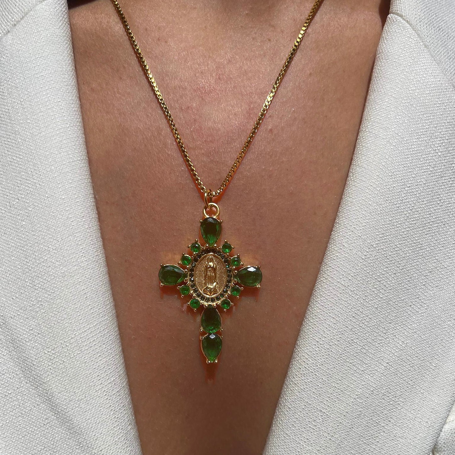 Colgante Cruz Circonitas Verdes de Bendita Eva en acero y oro lucido en modelo. Circonitas verdes de 2,5 mm con virgen grabada, cadena ajustable 40-45 cm, diseño moderno, waterproof y hipoalergénico.