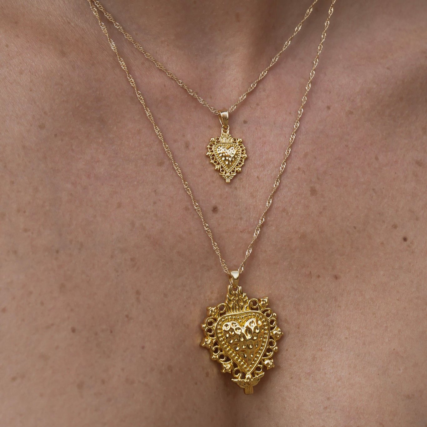 Modelo luciendo colgantes Sagrado Corazón Fe de 2 y 4 cm de Bendita Eva en oro, combinados en layering, joyas de la colección Bendita.
