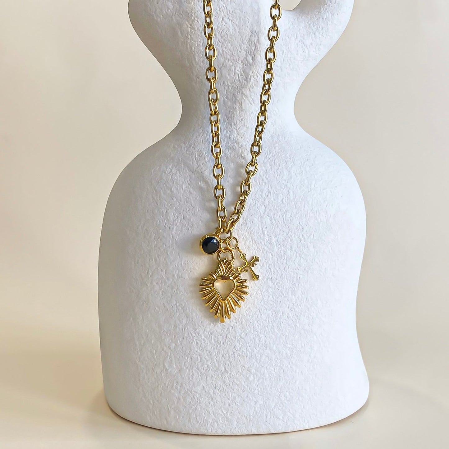 Collar waterproof de Bendita Eva en acero y oro mostrado en busto. Incluye corazón, cruz mini y charm con piedra negra. Ajustable 40-45 cm, diseño elegante, perfecto para looks de tendencia.