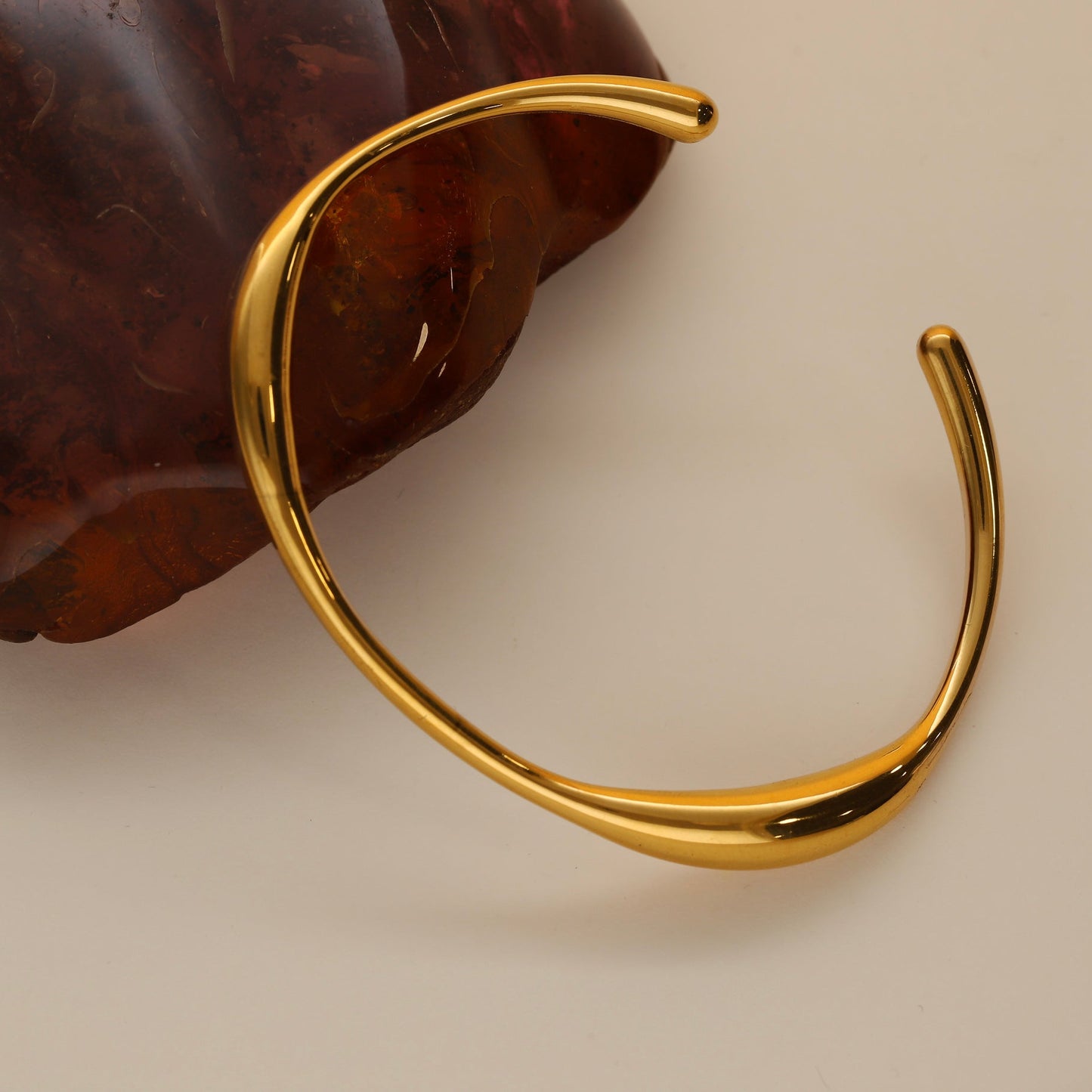 Pulsera rígida Viena de Bendita Eva en dorado waterproof, mostrada sobre piedra roja burdeos, destacando su diseño orgánico y sofisticado.
